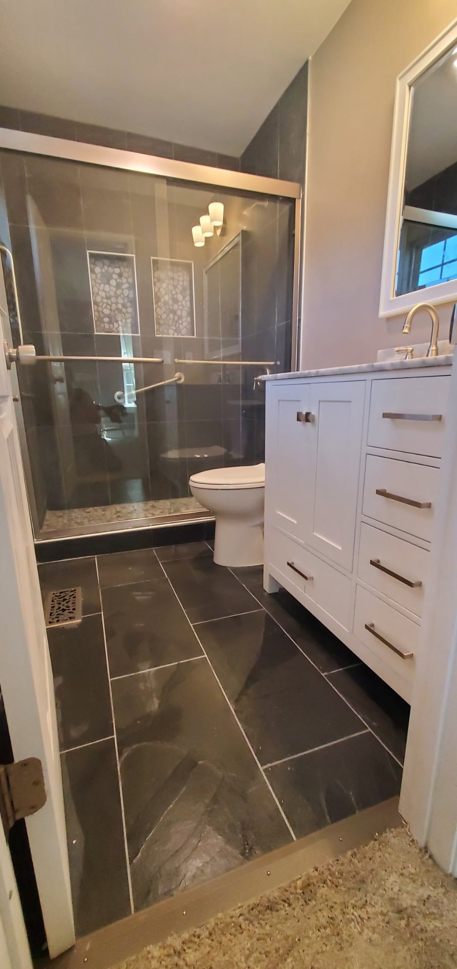 Completed gray tile bathroom with glass shower, white vanity and dark tile floor