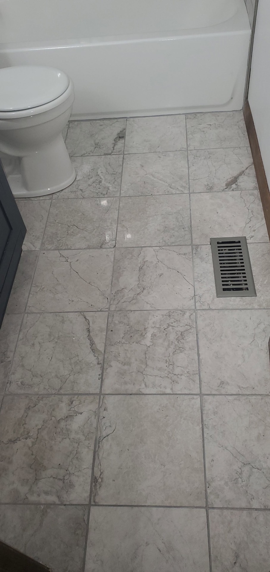 Marble-look porcelain tile floor installed in a bathroom with new baseboards and floor vent
