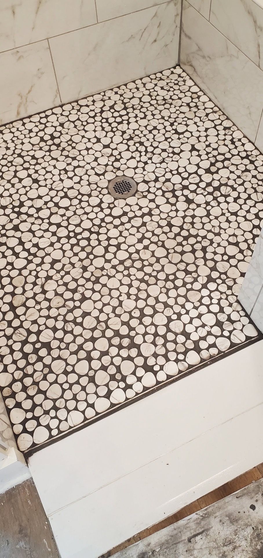 Pebble mosaic tile shower floor with centered drain and marble-look wall tile