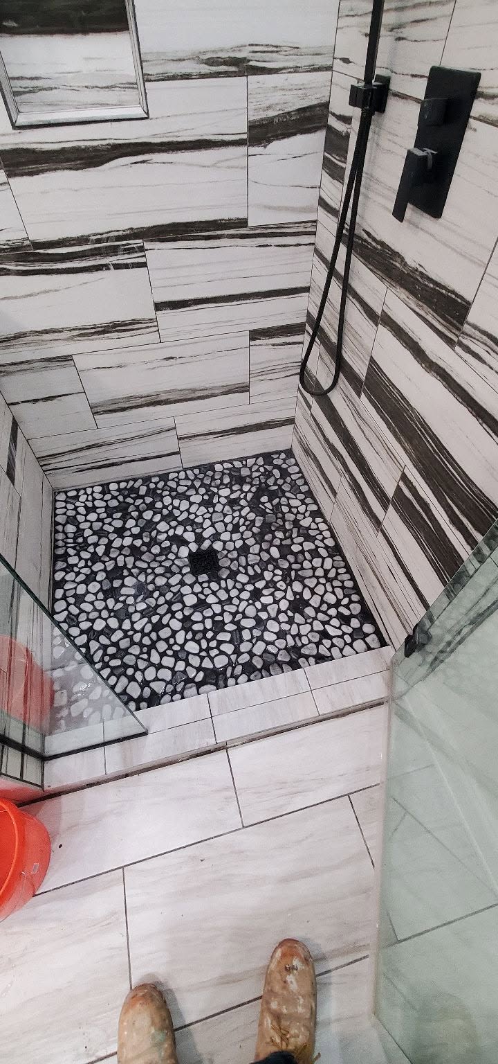 Walk-in tile shower with matte black fixtures and pebble stone floor