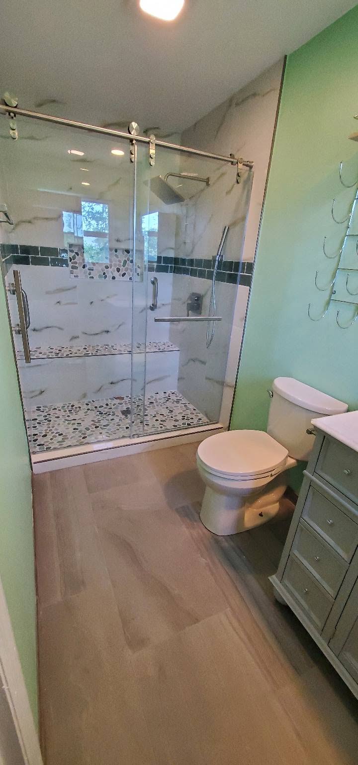 Bright bathroom remodel with frameless glass shower, pebble tile and gray vanity